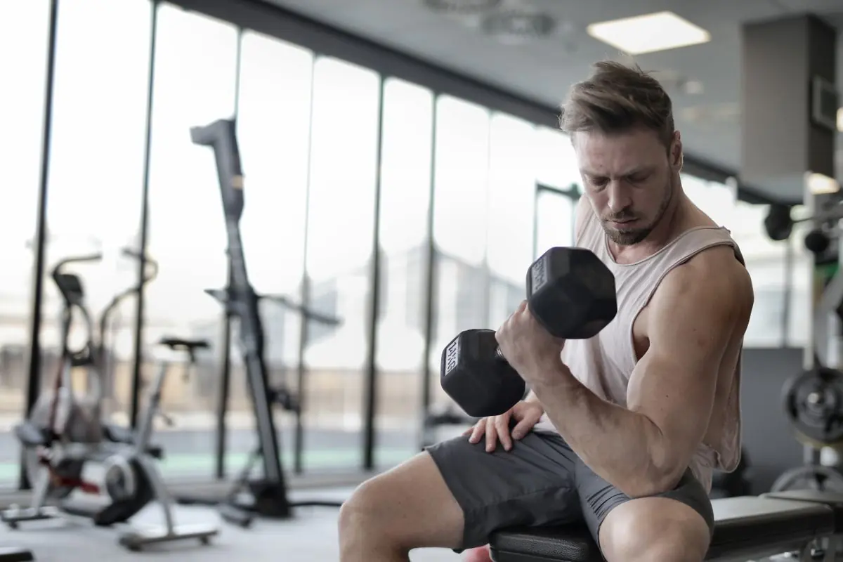 Man training with a dumbbell beside a window in a daylit gym