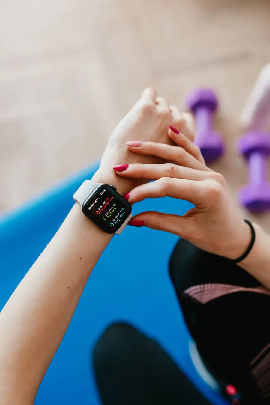 Checking a workout timer on a watch beside a pair of dumbbells